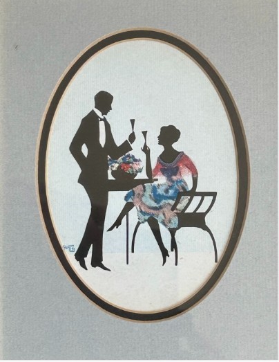 An Art Deco framed silhouette picture featuring a couple holding glasses, set within an oval mount and a wide burr wood frame. View III