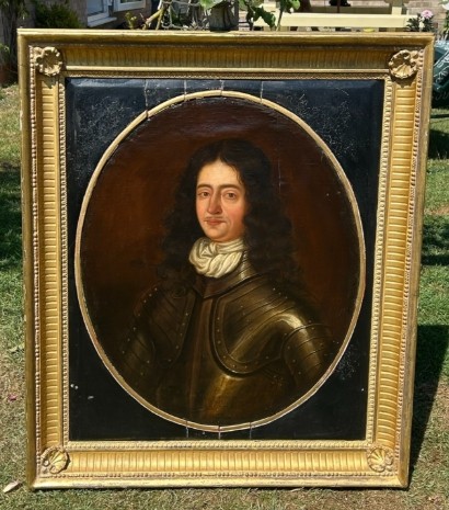 A seventeenth-century oil painting on canvas depicting a gentleman in dark plate armour, set within an oval spandrel inside a decorative giltwood frame.