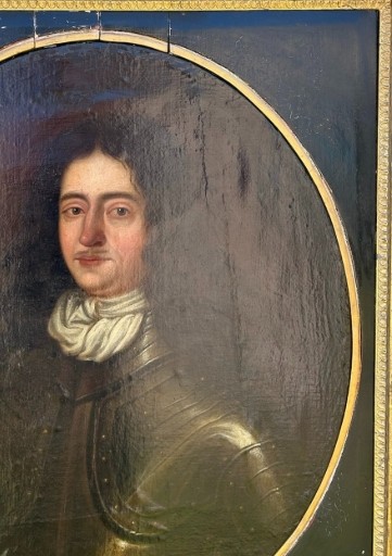 A seventeenth-century oil painting on canvas depicting a gentleman in dark plate armour, set within an oval spandrel inside a decorative giltwood frame. View V