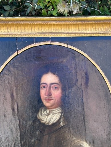 A seventeenth-century oil painting on canvas depicting a gentleman in dark plate armour, set within an oval spandrel inside a decorative giltwood frame. View VI