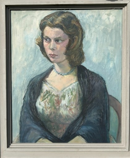 A mid-century oil painting on canvas depicting a seated woman wearing a patterned dress, blue necklace, and dark shawl, framed in a grey wooden frame. View VIII