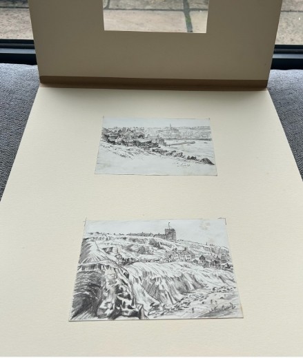 A pair of mounted monochrome graphite pencil drawings depicting coastal buildings and cliffs in Whitby, signed and dated 1934. View VII