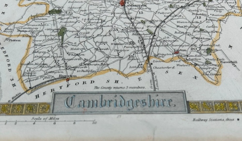 A hand-coloured 19th-century engraved map of Cambridgeshire by Thomas Moule framed by Gothic architectural borders, heraldic shields, and vignettes of Ely Cathedral and Wimpole Hall. View II