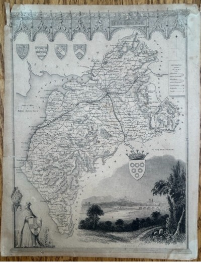 A nineteenth-century monochrome steel engraving map of Cumberland by Thomas Moule featuring decorative Gothic tracery borders, coats of arms, and an architectural vignette of Carlisle.