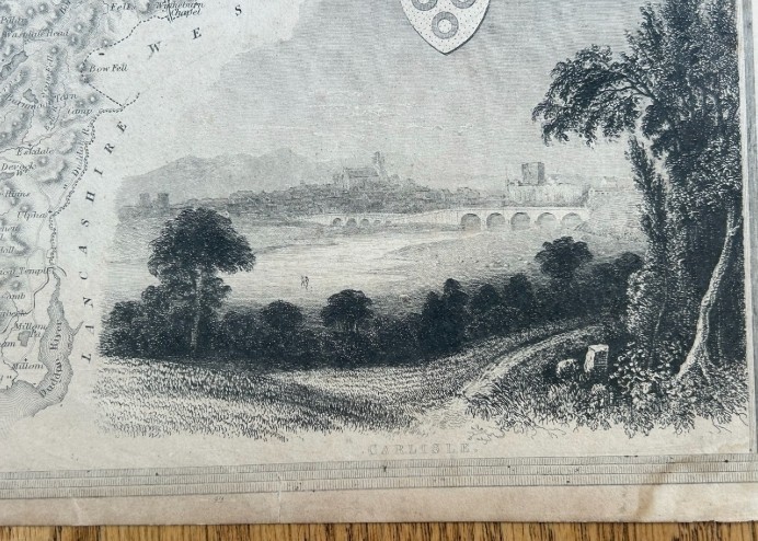 A nineteenth-century monochrome steel engraving map of Cumberland by Thomas Moule featuring decorative Gothic tracery borders, coats of arms, and an architectural vignette of Carlisle. View III