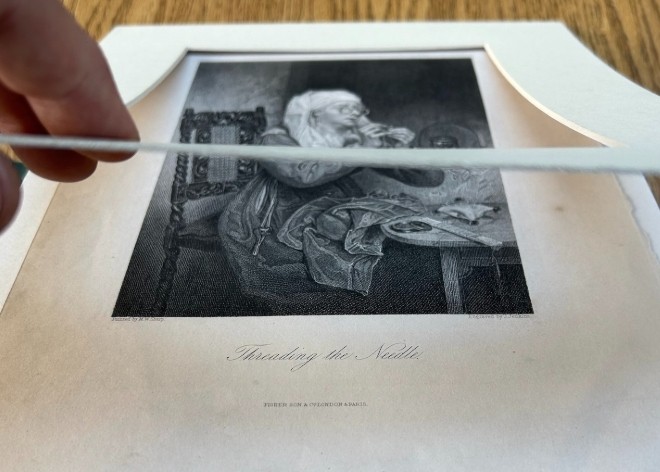 A monochrome nineteenth-century steel engraving depicting an elderly woman wearing spectacles and a headscarf threading a needle while seated at a small wooden table. View VIII