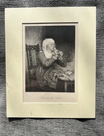 A monochrome nineteenth-century steel engraving depicting an elderly woman wearing spectacles and a headscarf threading a needle while seated at a small wooden table. View X