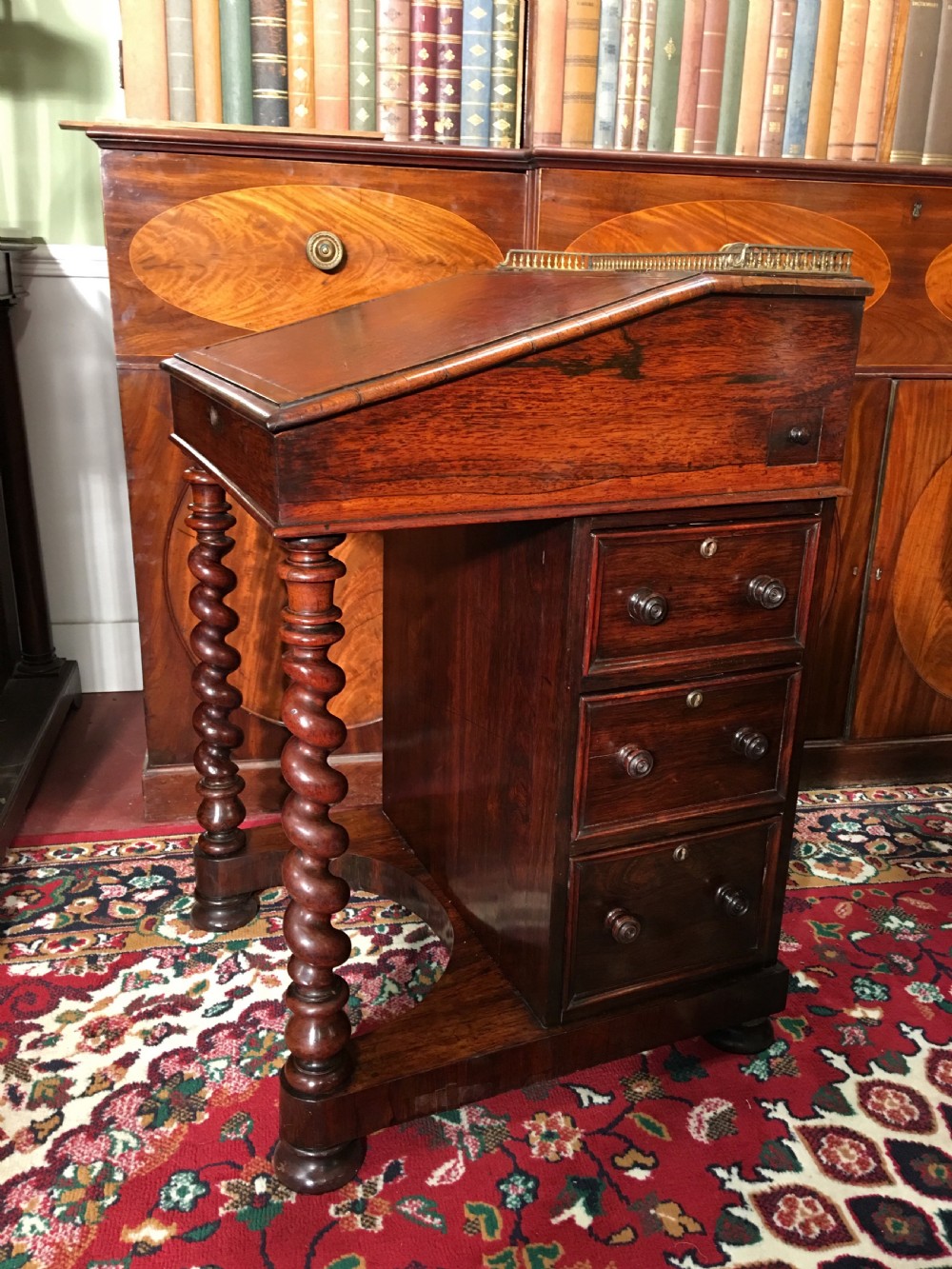 A William IV dark rosewood Davenport writing desk featuring carved barley twist front supports, a sloped writing top, a brass gallery, and side-opening drawers.