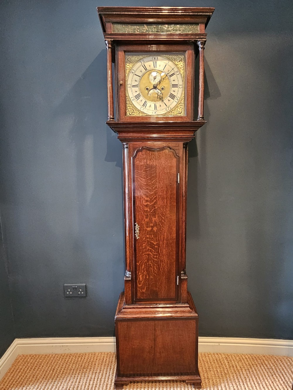 An antique Georgian oak longcase clock featuring a square brass dial, turned hood columns, and an arched trunk door.