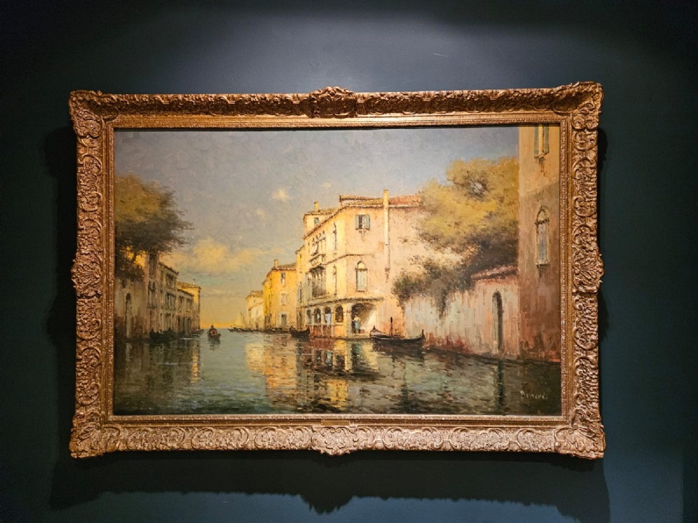 An oil on canvas landscape painting depicting a Venetian canal with gondolas and historic buildings, framed in an ornate gilded wood frame.