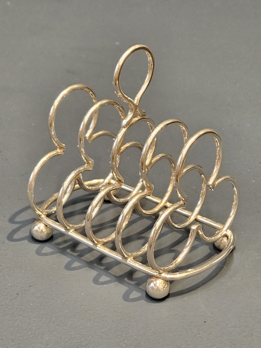 A Victorian silver toast rack featuring five trefoil-shaped wire dividers, a central loop handle, and spherical ball feet.