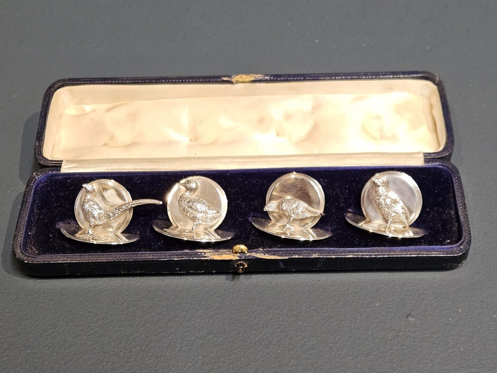 A set of four Edwardian silver menu holders shaped like game birds, presented inside a dark blue velvet-lined case.