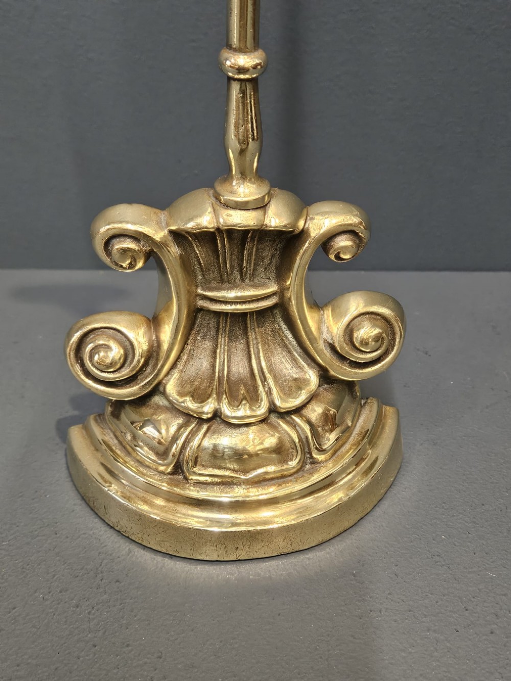 A Regency style polished brass door stop featuring a decorative scrolled base, a tall turned stem, and an oval ring handle. View IV