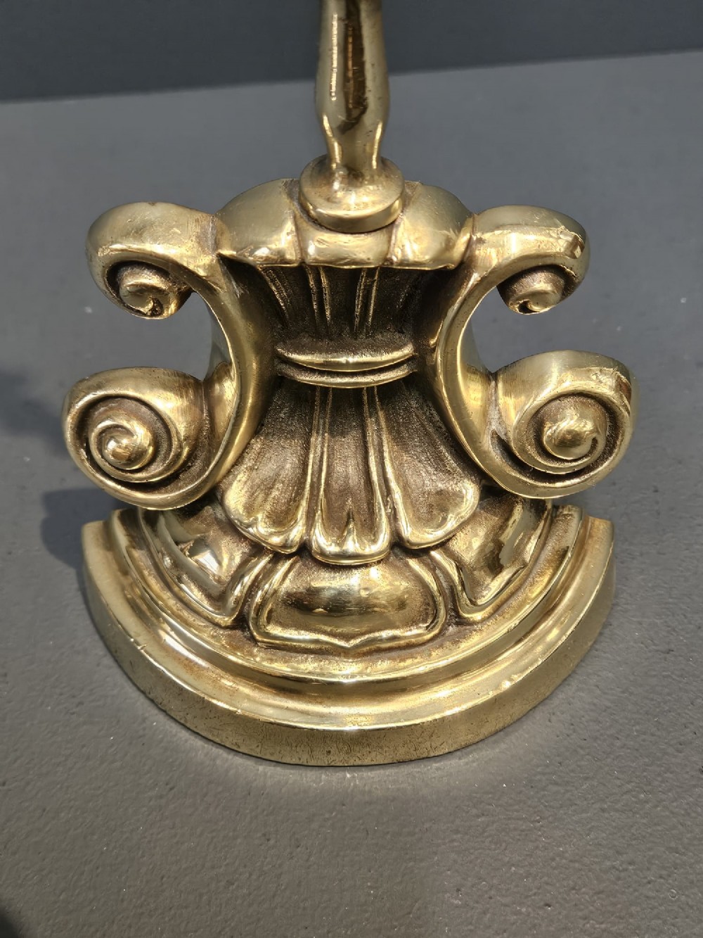 A Regency style polished brass door stop featuring a decorative scrolled base, a tall turned stem, and an oval ring handle. View V