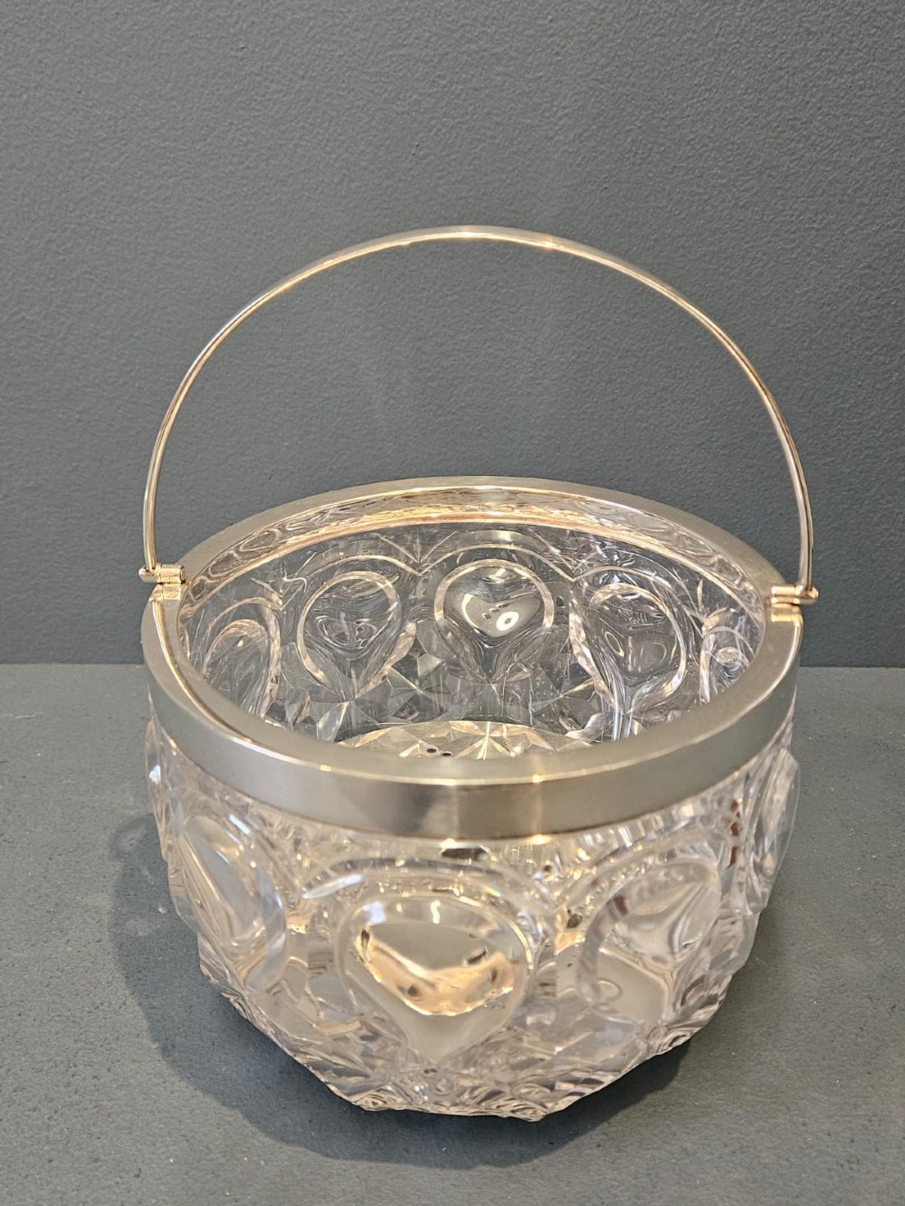 A clear cut crystal ice pail featuring an arched decorative motif, fitted with a silver rim and a slender swing handle. View II
