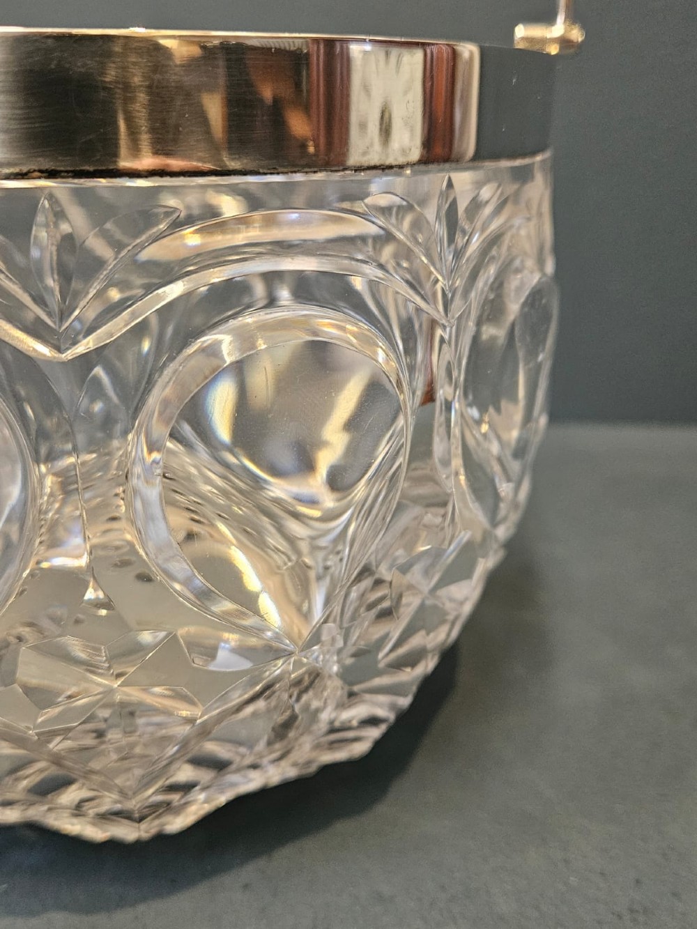 A clear cut crystal ice pail featuring an arched decorative motif, fitted with a silver rim and a slender swing handle. View III