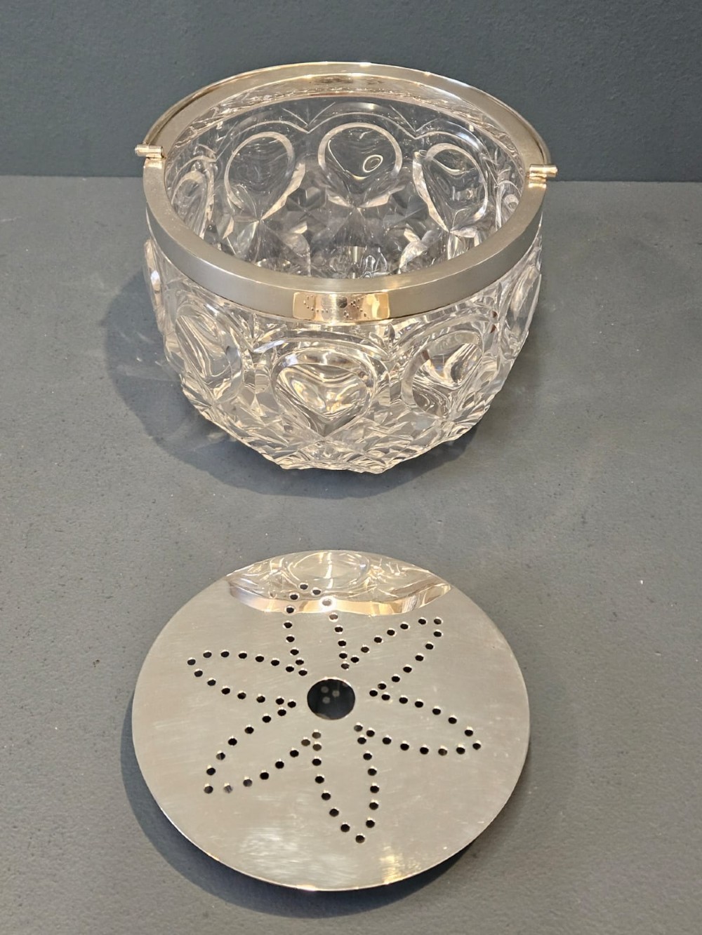A clear cut crystal ice pail featuring an arched decorative motif, fitted with a silver rim and a slender swing handle. View IV