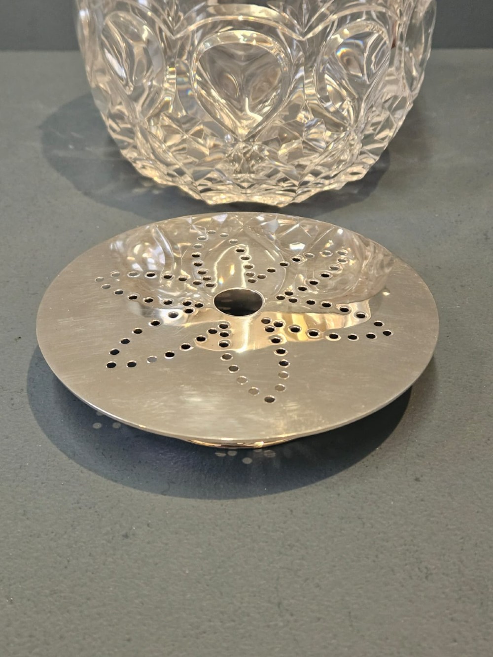 A clear cut crystal ice pail featuring an arched decorative motif, fitted with a silver rim and a slender swing handle. View V