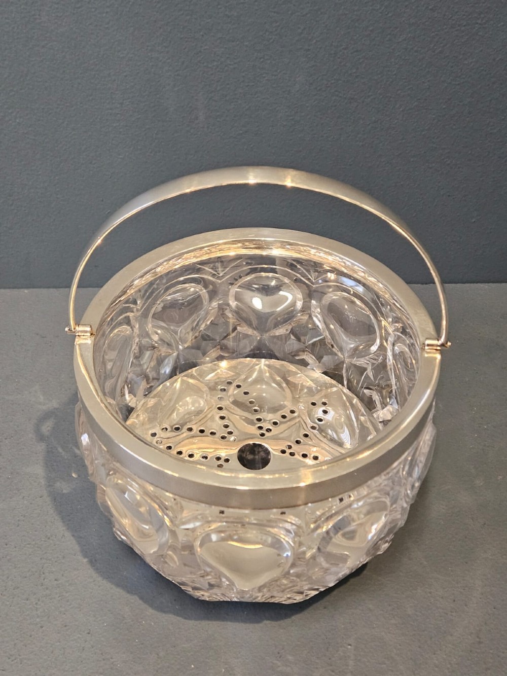 A clear cut crystal ice pail featuring an arched decorative motif, fitted with a silver rim and a slender swing handle. View VI