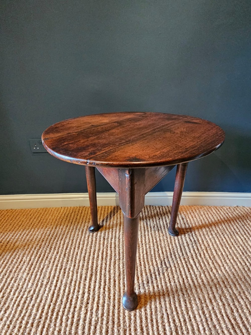 A round Georgian elm cricket table with three tapered legs terminating in pad feet and a triangular deep apron.