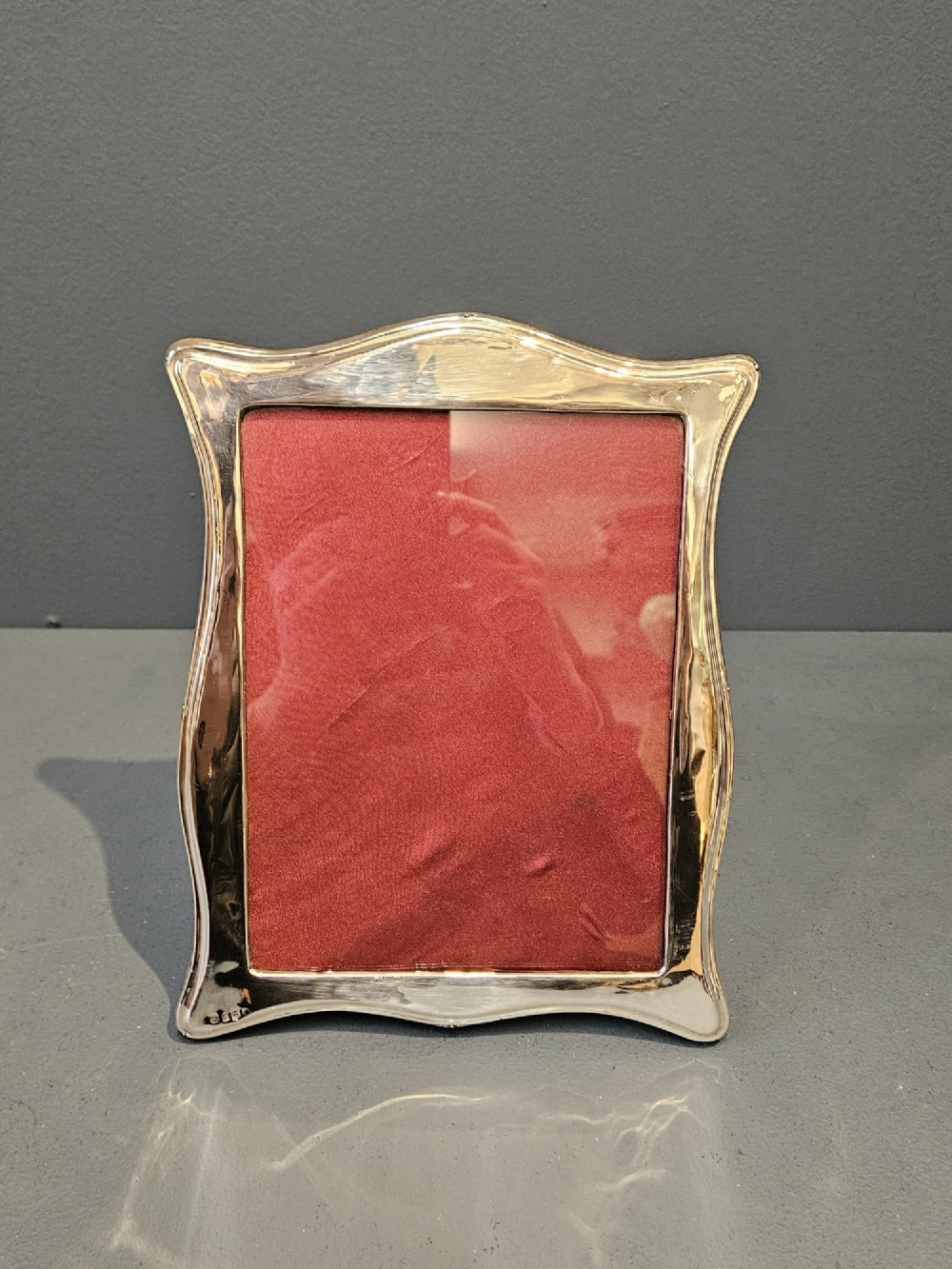 A hallmarked silver portrait photo frame featuring a curved border and a red backing.