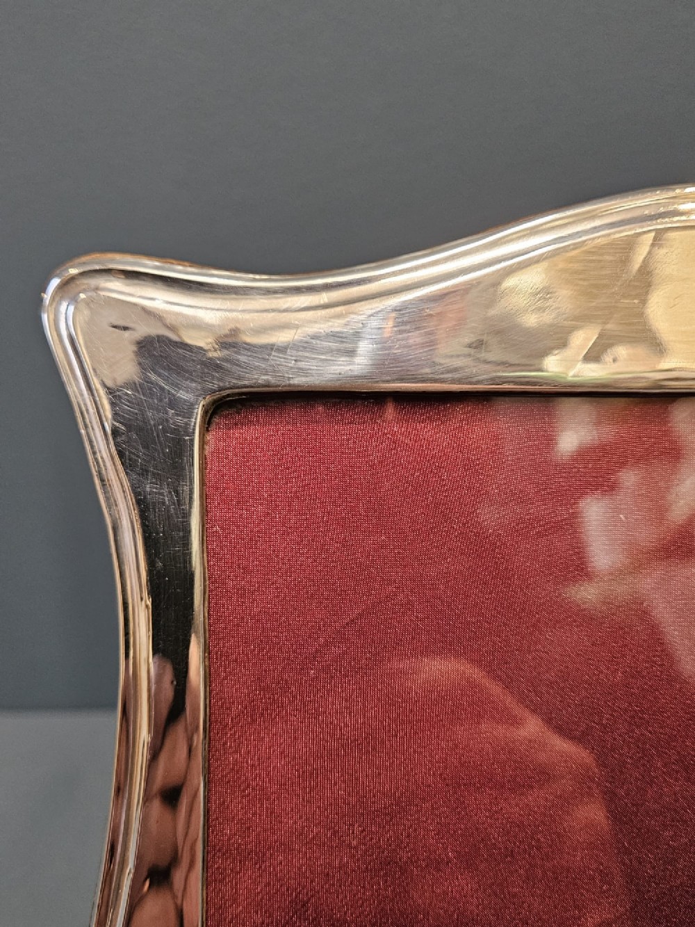 A hallmarked silver portrait photo frame featuring a curved border and a red backing. View II