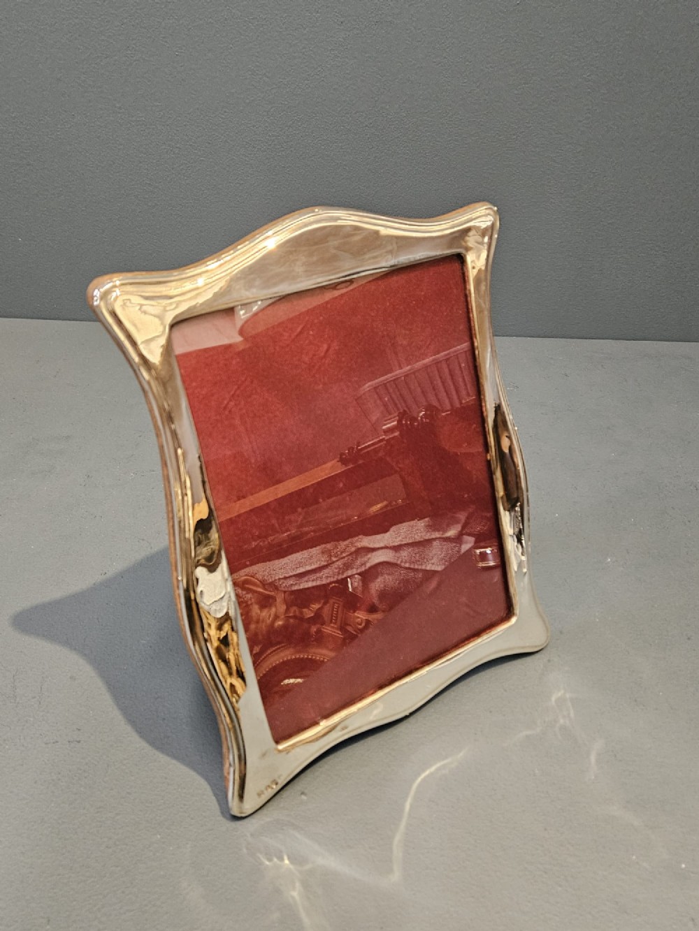 A hallmarked silver portrait photo frame featuring a curved border and a red backing. View V