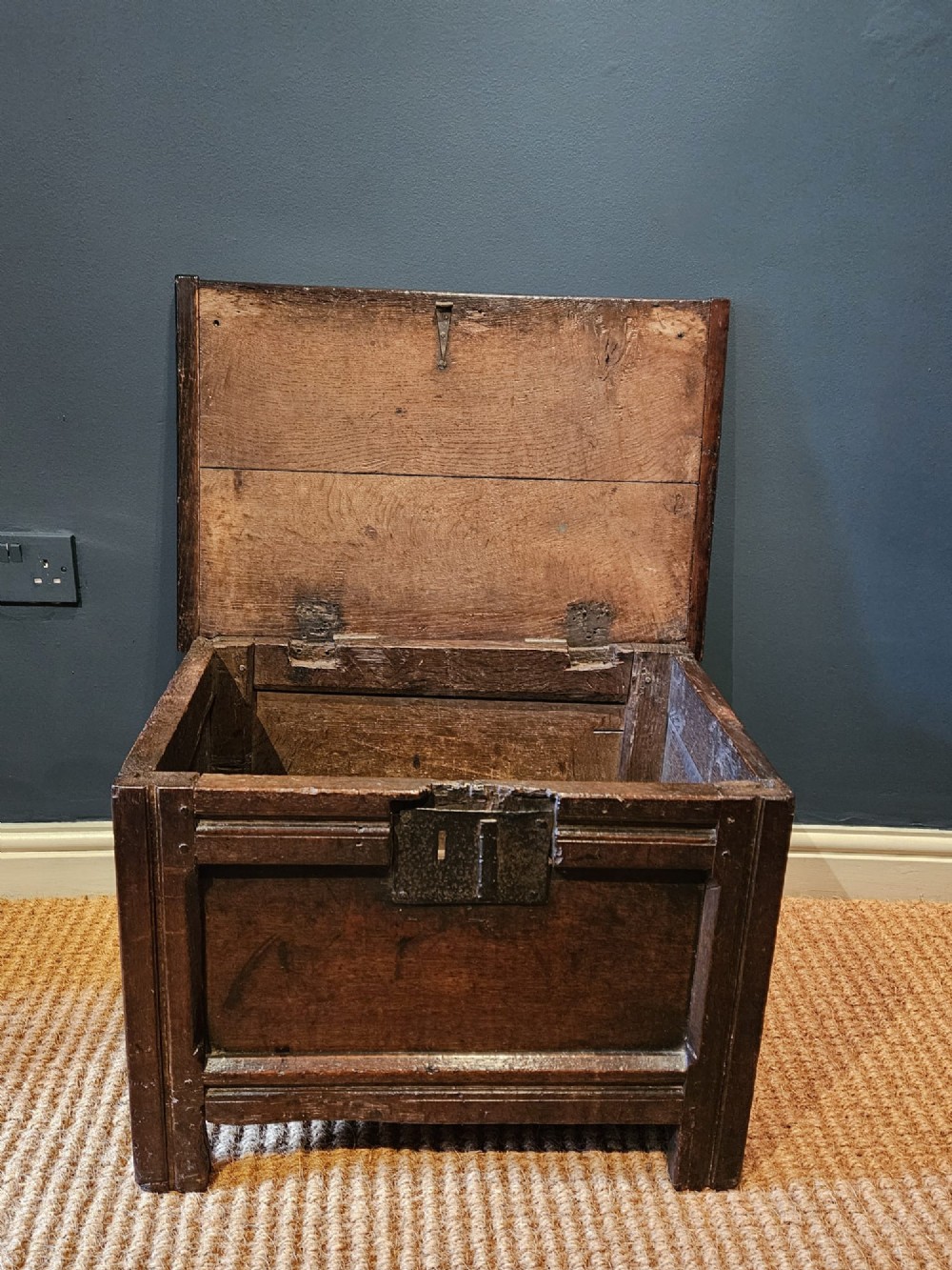 A small 17th-century dark oak coffer featuring a single front panel, a hinged plank top, and a wrought iron lock plate. View IV