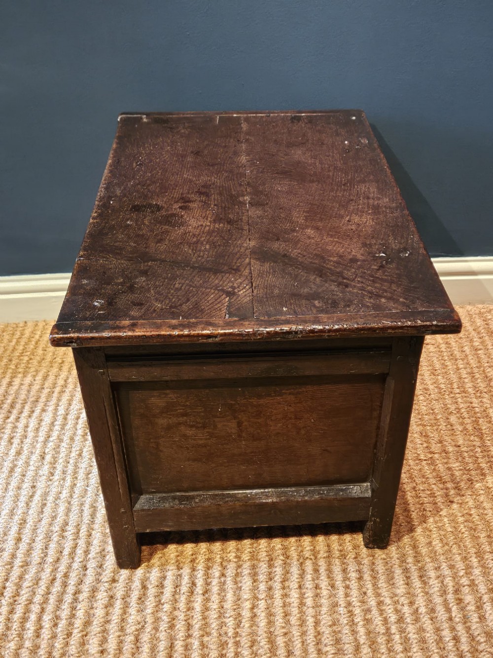 A small 17th-century dark oak coffer featuring a single front panel, a hinged plank top, and a wrought iron lock plate. View VII