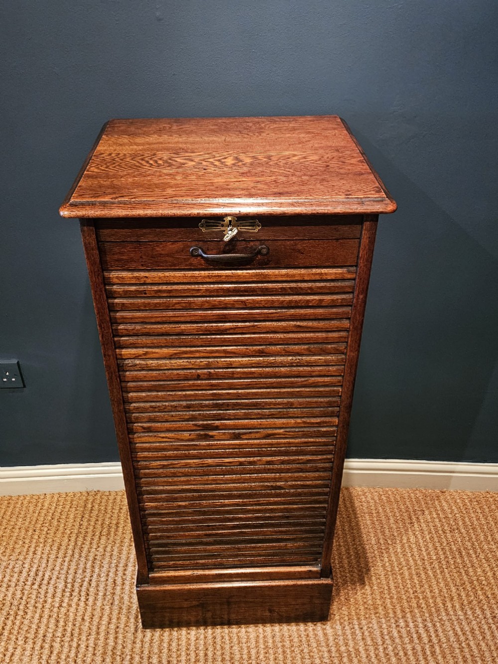A tall Victorian medium brown oak filing cabinet featuring internal document trays with brass label holders and a top key lock. View III