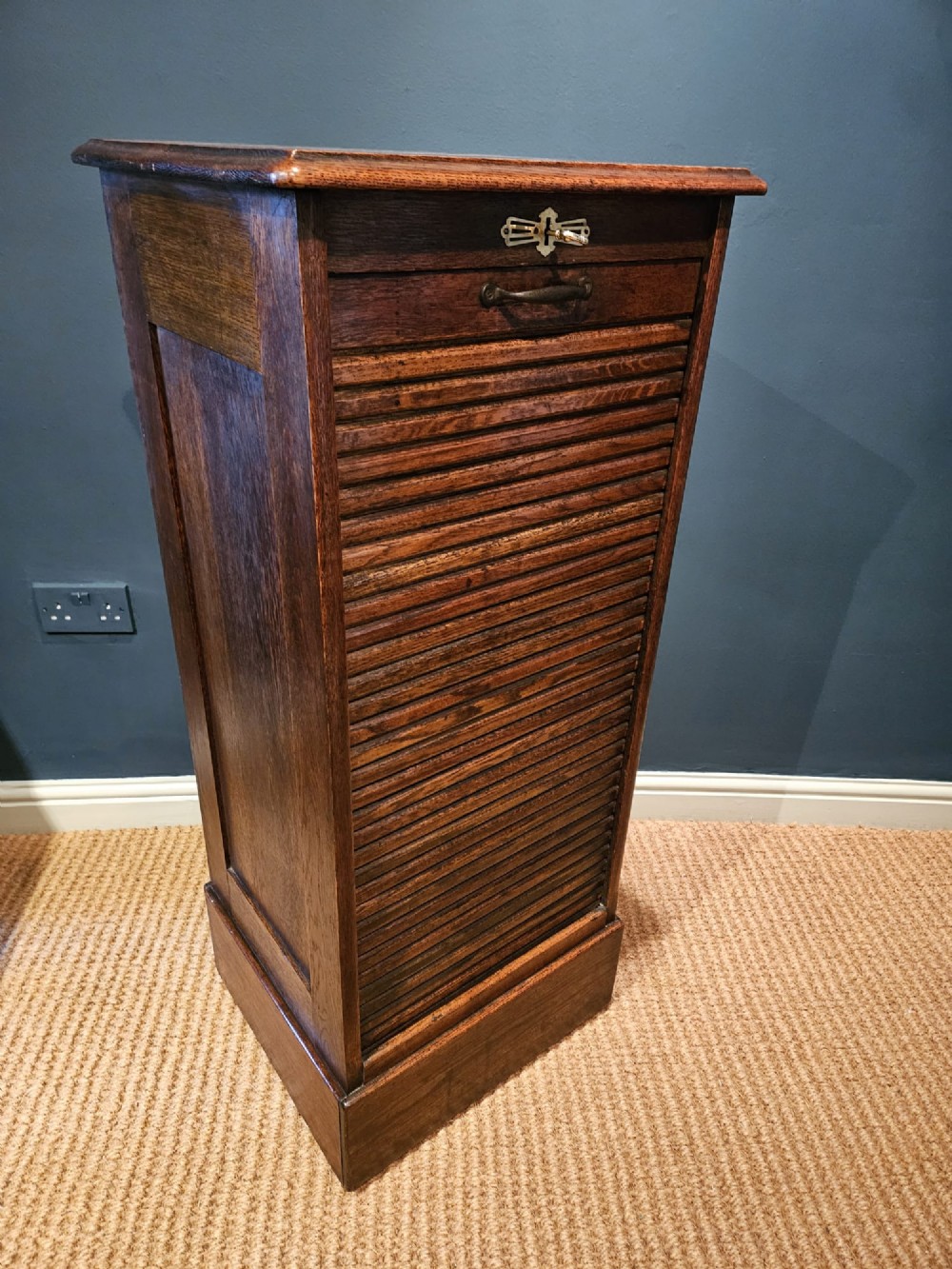 A tall Victorian medium brown oak filing cabinet featuring internal document trays with brass label holders and a top key lock. View V