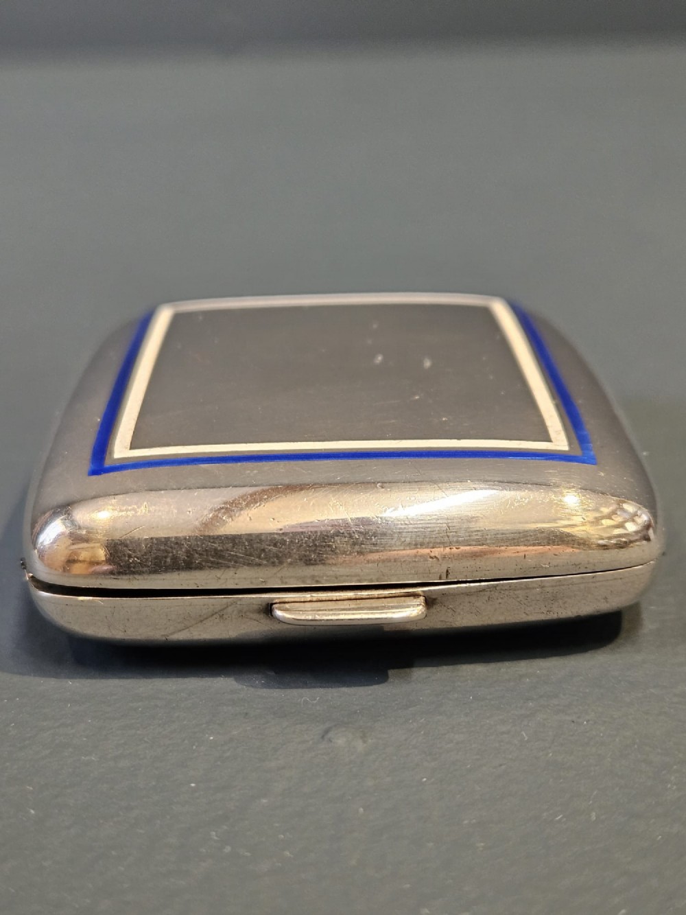 A squarish sterling silver pocket watch case with rounded corners, featuring a blue and white enamel border around the top lid and a thumbpiece latch.