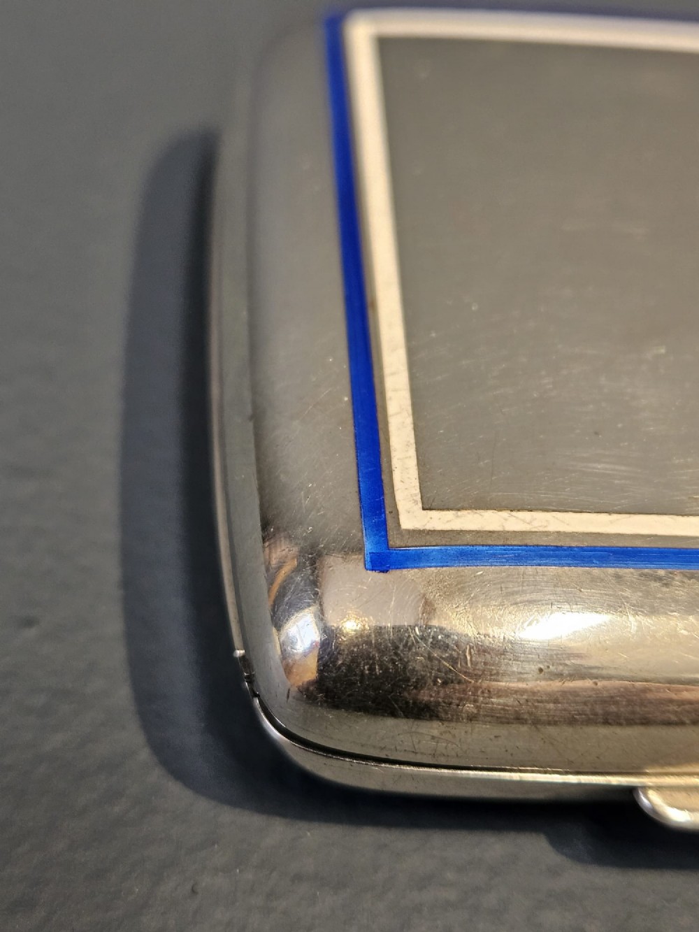A squarish sterling silver pocket watch case with rounded corners, featuring a blue and white enamel border around the top lid and a thumbpiece latch. View II