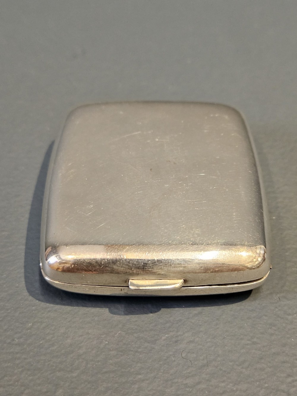 A squarish sterling silver pocket watch case with rounded corners, featuring a blue and white enamel border around the top lid and a thumbpiece latch. View III
