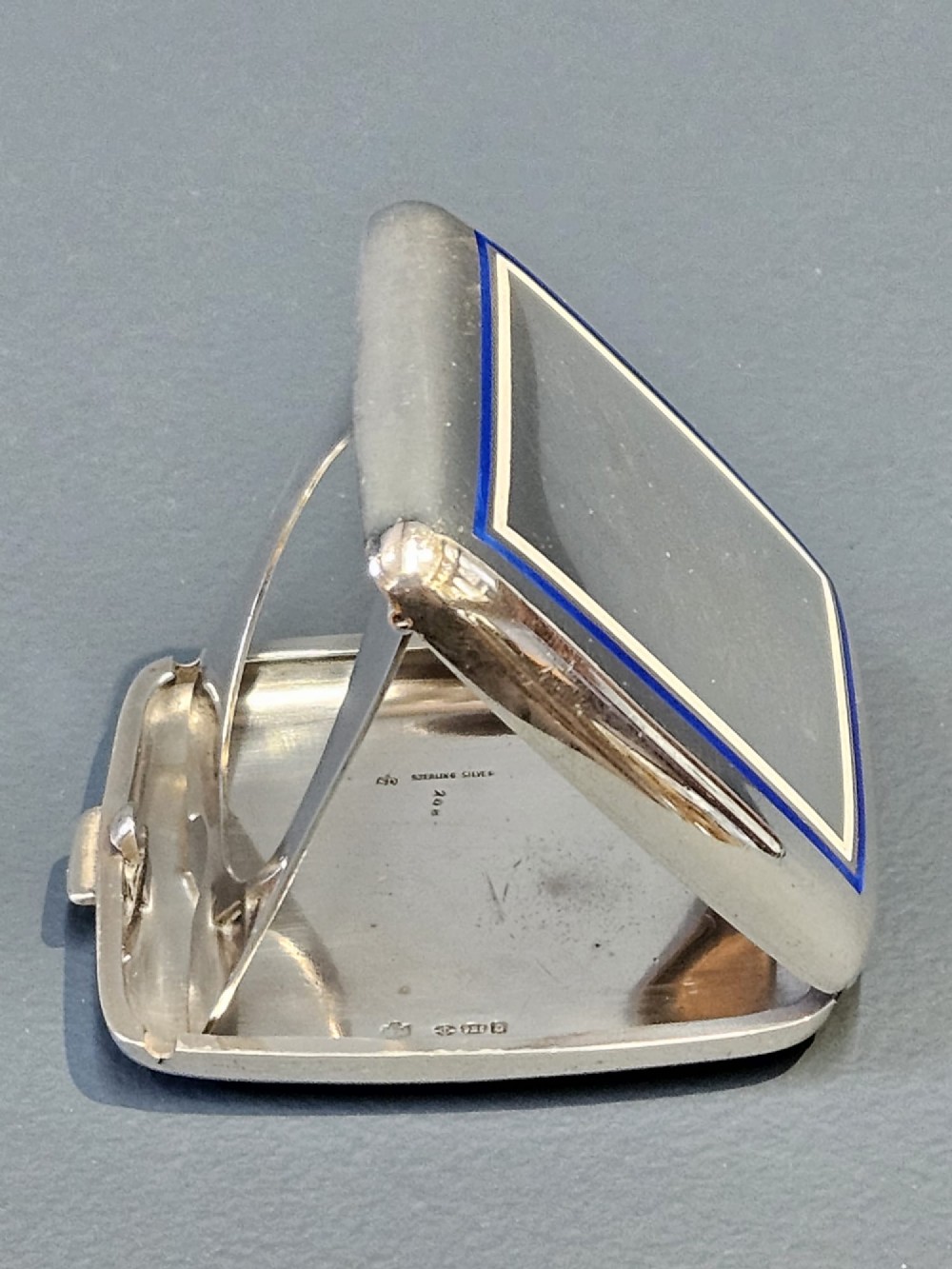 A squarish sterling silver pocket watch case with rounded corners, featuring a blue and white enamel border around the top lid and a thumbpiece latch. View V