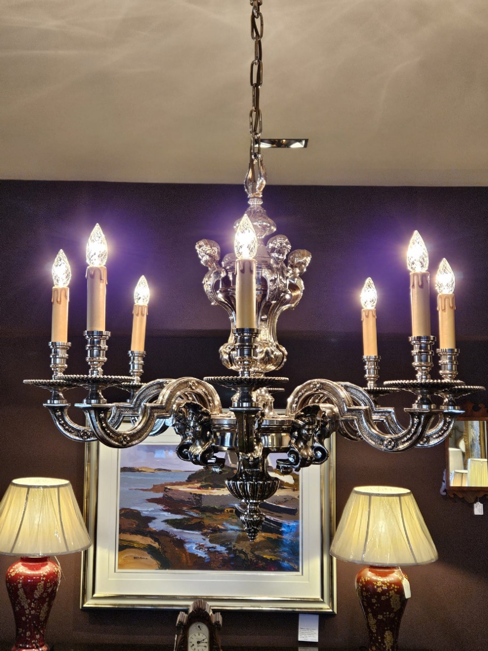 An Edwardian eight-arm nickel-plated chandelier featuring decorative central baluster detailing, S-scroll branches, and faux candle sleeves.