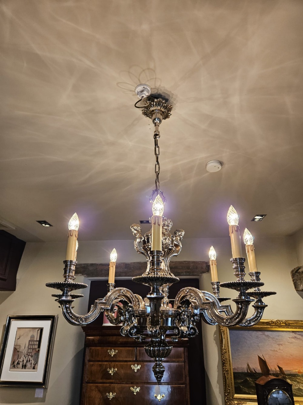 An Edwardian eight-arm nickel-plated chandelier featuring decorative central baluster detailing, S-scroll branches, and faux candle sleeves. View II