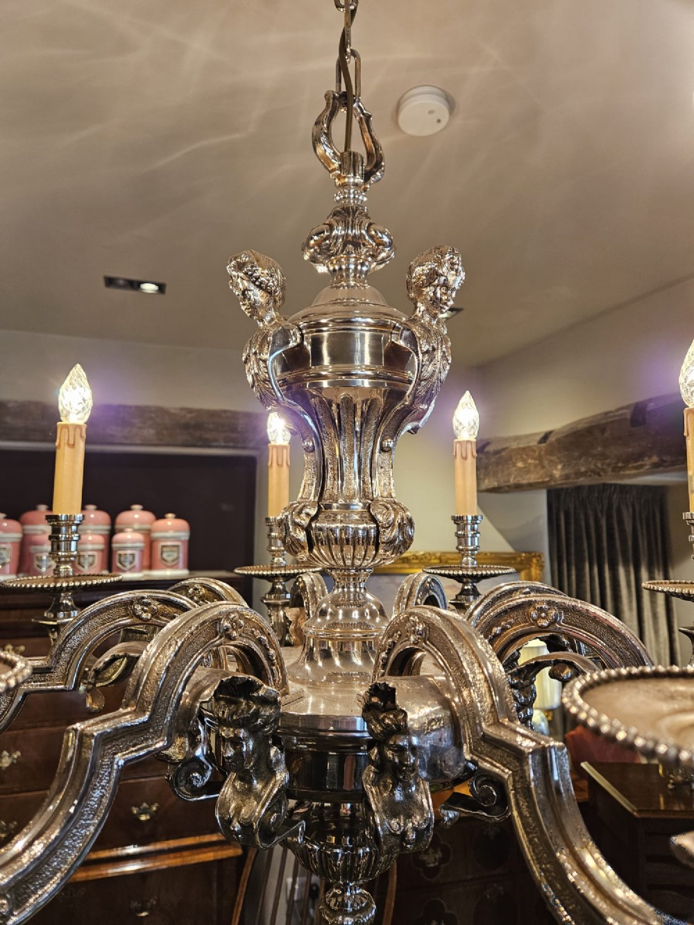 An Edwardian eight-arm nickel-plated chandelier featuring decorative central baluster detailing, S-scroll branches, and faux candle sleeves. View IV