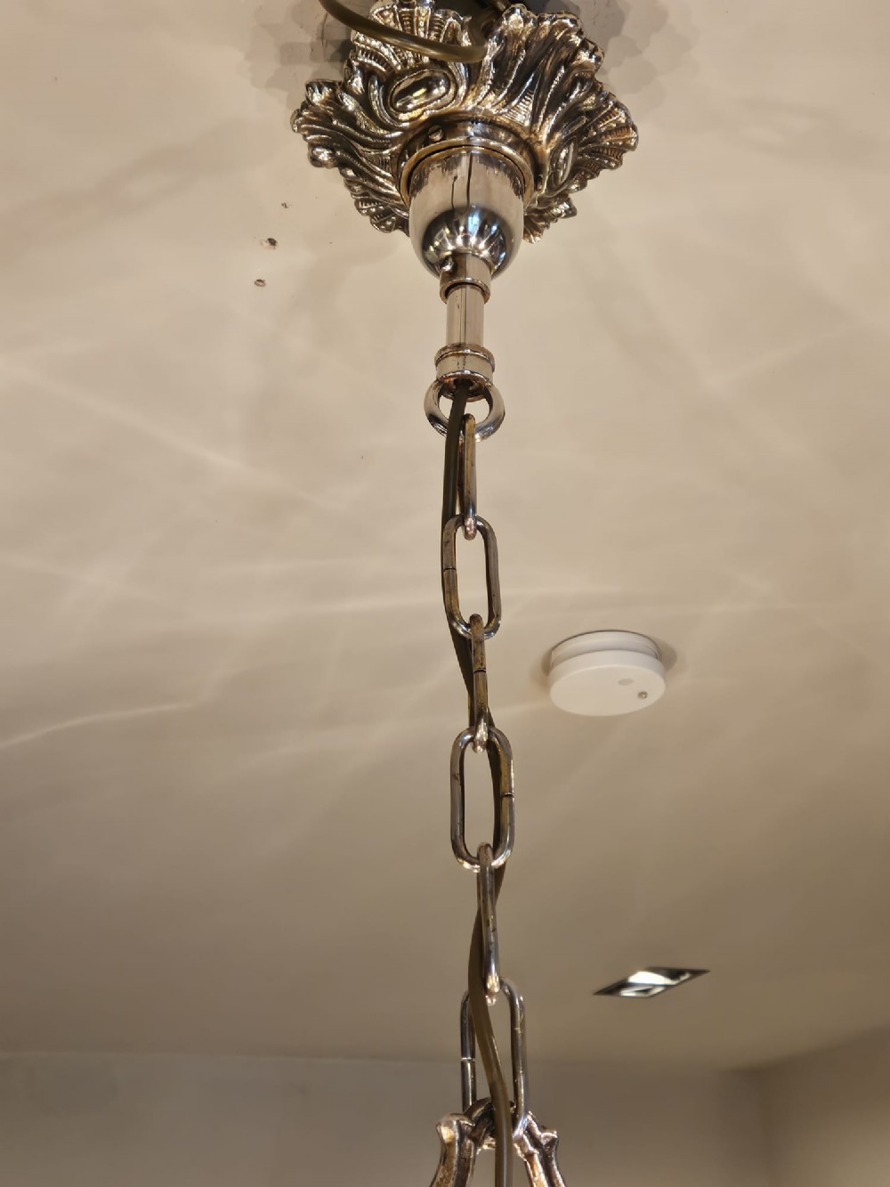 An Edwardian eight-arm nickel-plated chandelier featuring decorative central baluster detailing, S-scroll branches, and faux candle sleeves. View VI