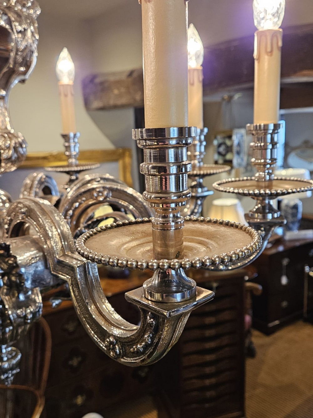 An Edwardian eight-arm nickel-plated chandelier featuring decorative central baluster detailing, S-scroll branches, and faux candle sleeves. View VIII