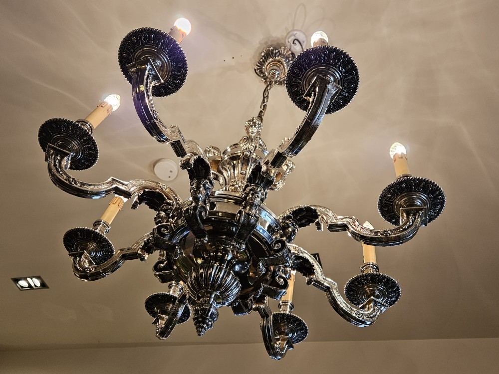 An Edwardian eight-arm nickel-plated chandelier featuring decorative central baluster detailing, S-scroll branches, and faux candle sleeves. View IX