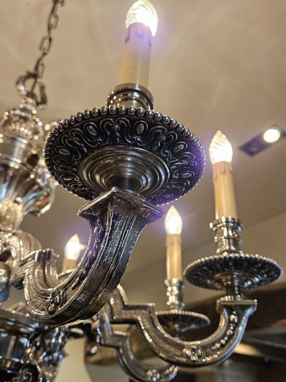 An Edwardian eight-arm nickel-plated chandelier featuring decorative central baluster detailing, S-scroll branches, and faux candle sleeves. View X