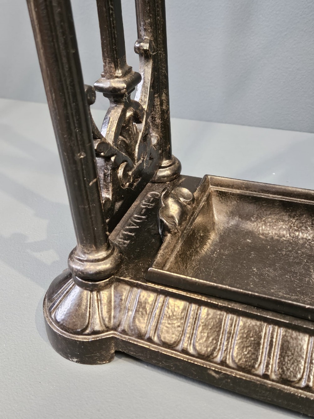 A rectangular Victorian cast iron stick stand featuring corner finials, multi-compartment top rail, vertical column supports, and a drip tray base. View III