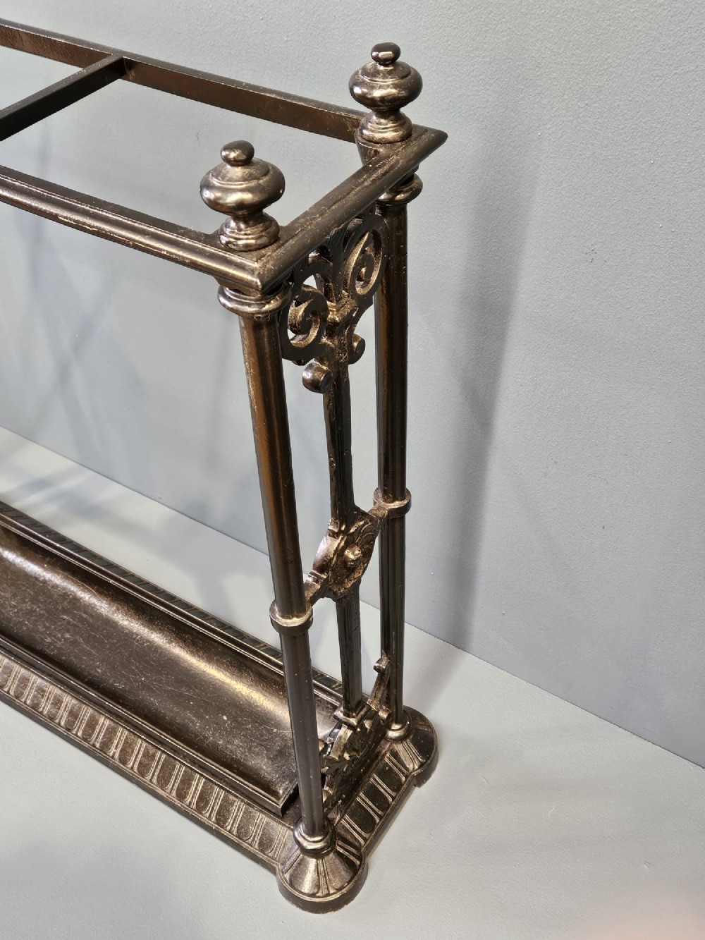 A rectangular Victorian cast iron stick stand featuring corner finials, multi-compartment top rail, vertical column supports, and a drip tray base. View V