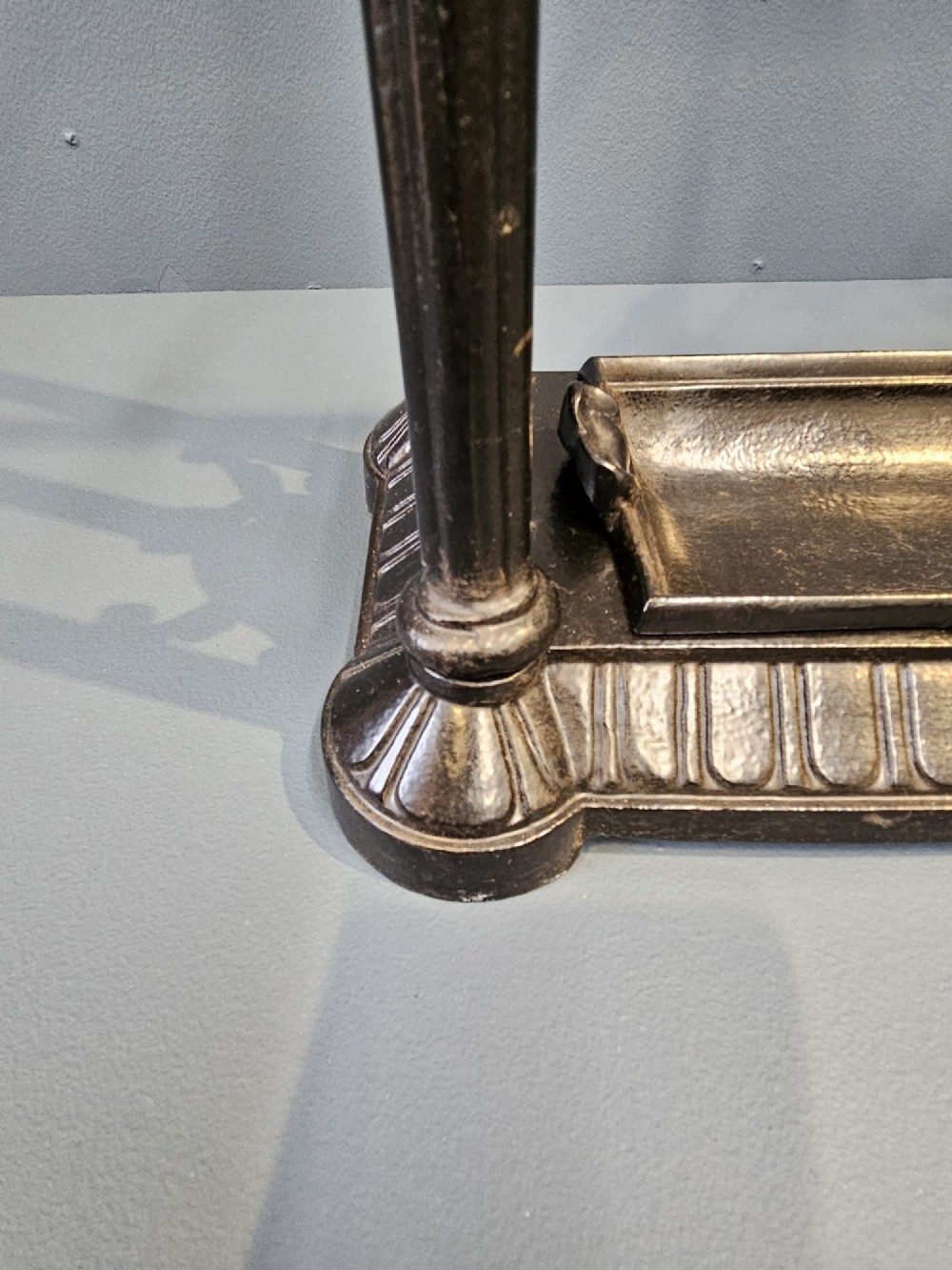 A rectangular Victorian cast iron stick stand featuring corner finials, multi-compartment top rail, vertical column supports, and a drip tray base. View VII