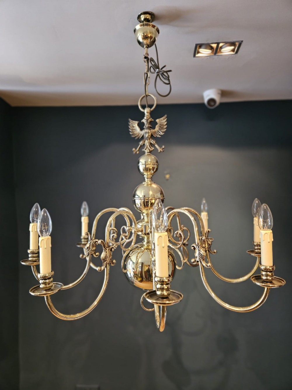 An Edwardian-style polished brass eight-arm chandelier featuring an eagle finial, central baluster stem, scrolling branches, and faux candle light sockets.