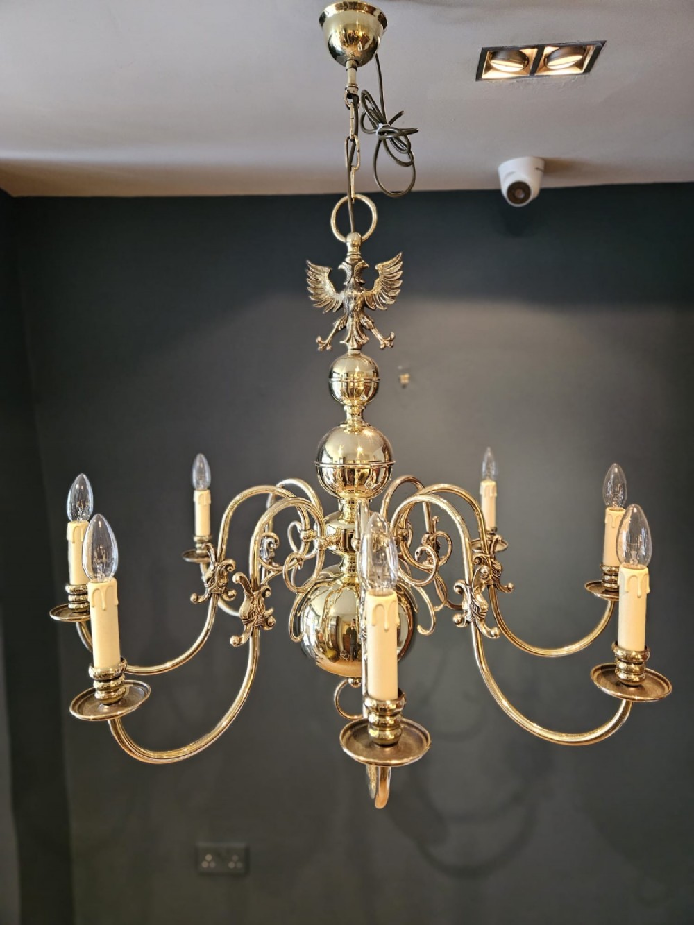 An Edwardian-style polished brass eight-arm chandelier featuring an eagle finial, central baluster stem, scrolling branches, and faux candle light sockets. View IV