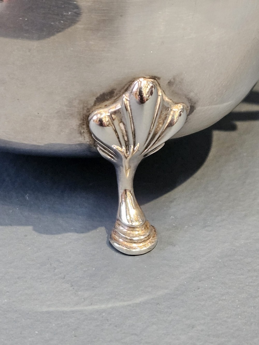 A George V polished sterling silver sauce boat featuring a wavy scalloped rim, a flying scroll handle, and three shell-capped feet. View III