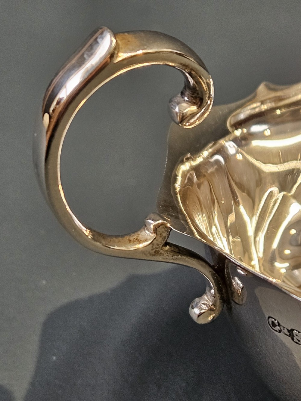 A George V polished sterling silver sauce boat featuring a wavy scalloped rim, a flying scroll handle, and three shell-capped feet. View V