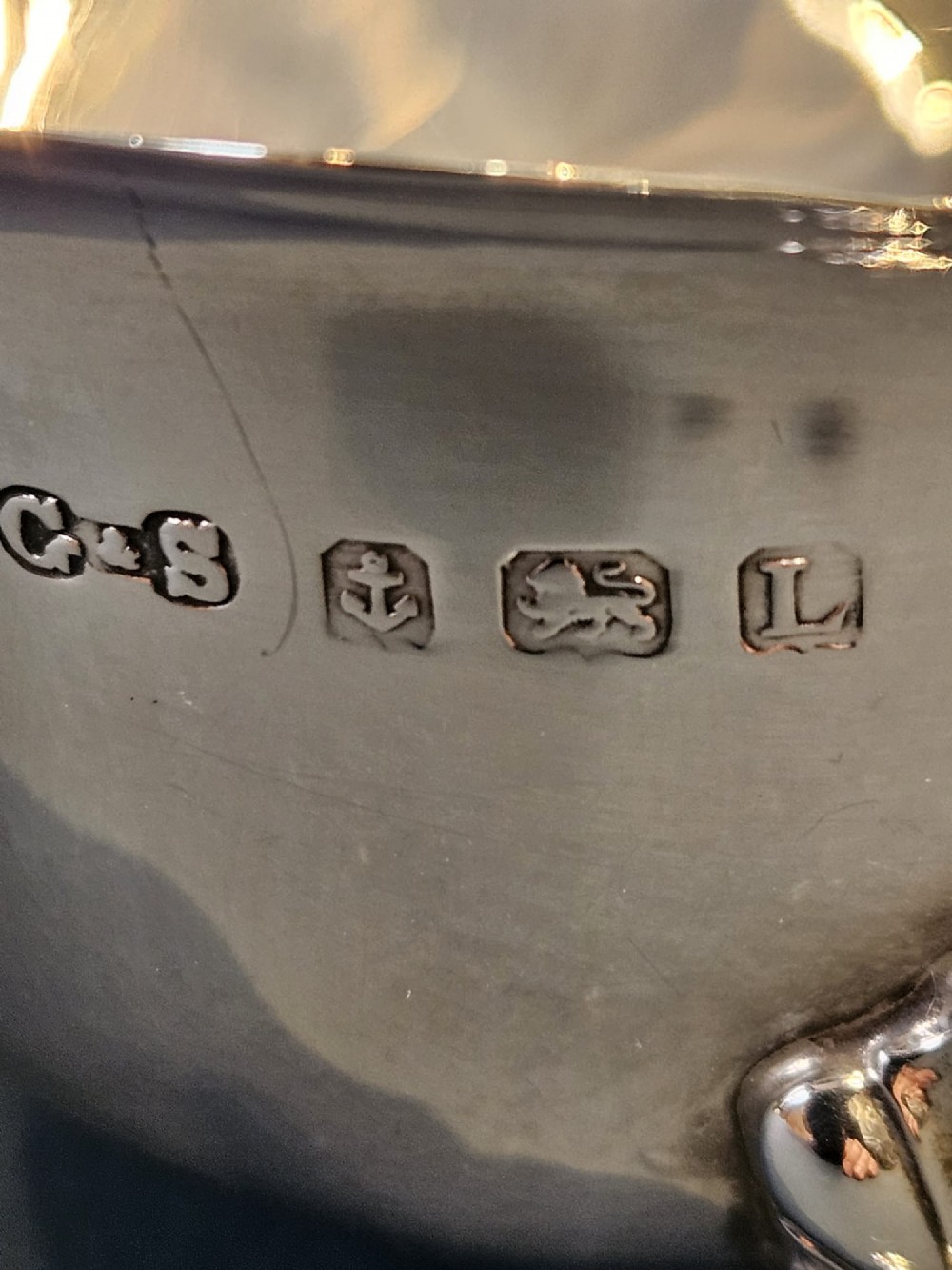 A George V polished sterling silver sauce boat featuring a wavy scalloped rim, a flying scroll handle, and three shell-capped feet. View VI